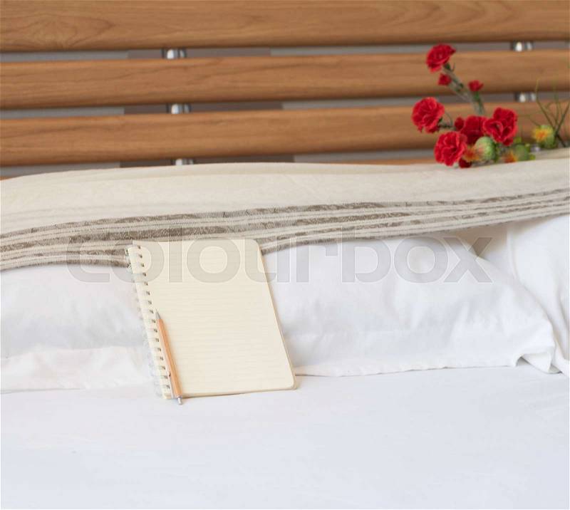 Notebook and wood pencil on white bed with flower bouquet background, stock photo