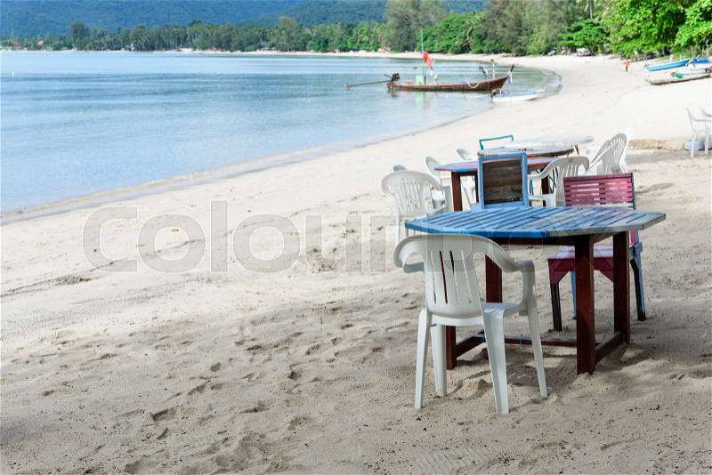 Wooden table and chair set on white beach sand and blue sea in sunny day, stock photo