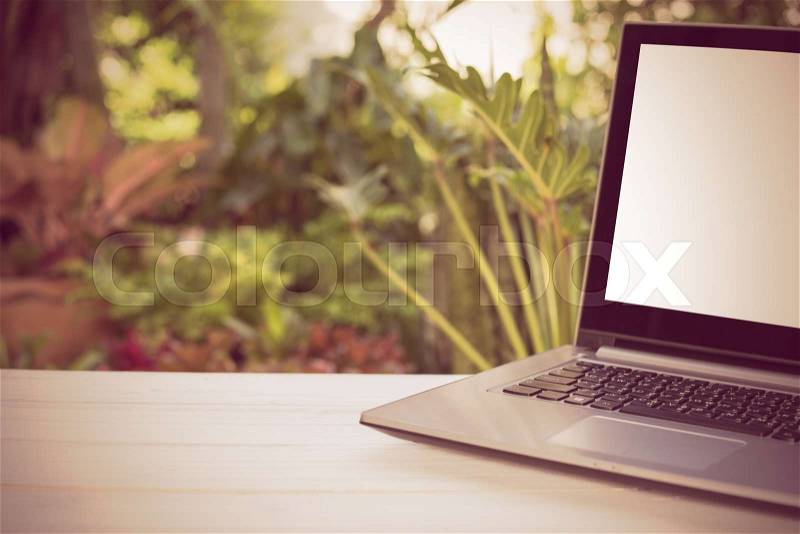 Computer laptop with blank white screen wooden table with green garden nature background,retro effect, stock photo