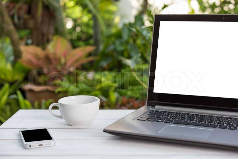 Computer laptop,mobile phone and coffee cup on white wooden table with green garden nature background, stock photo