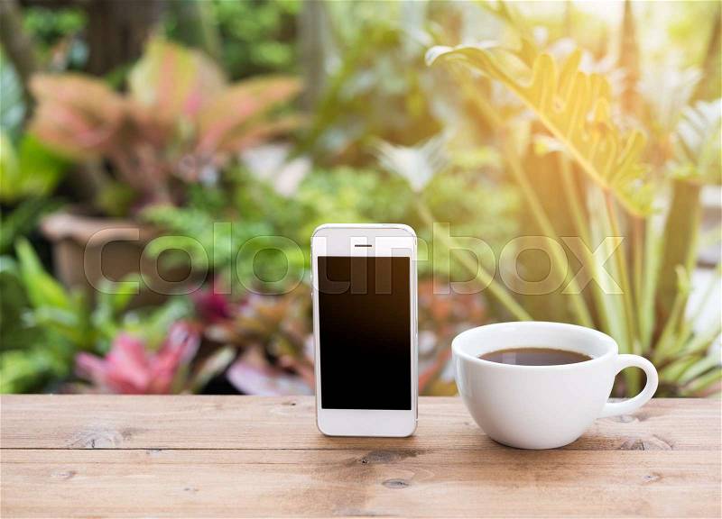 Morning outdoor work,coffee cup,mobile phone on wooden table in green garden background, stock photo