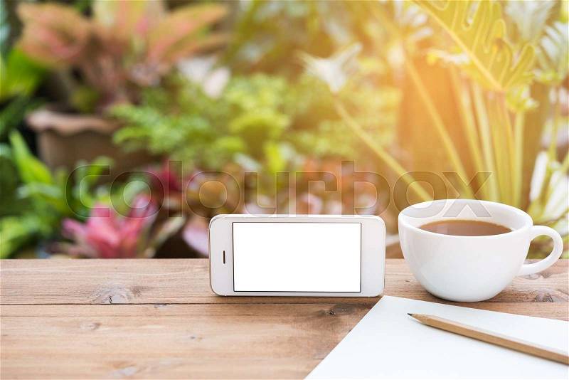 Morning outdoor work,coffee cup,mobile phone,paper and pencil on wooden table in green garden background, stock photo