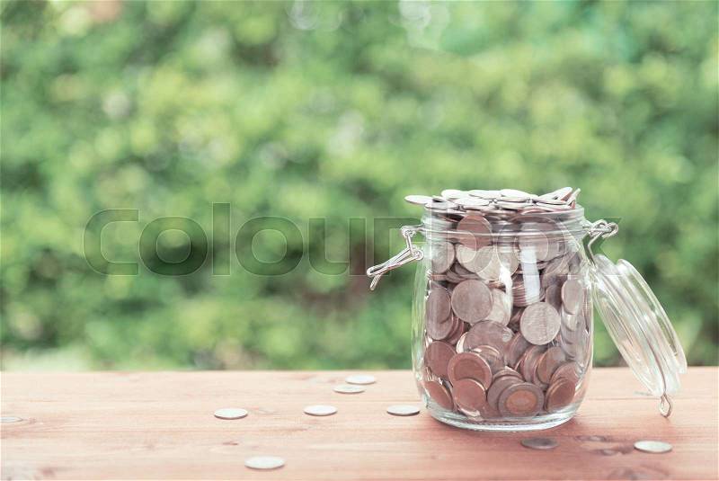 Money coins in glass jar on old wooden table with green nature background,saving money concept, stock photo