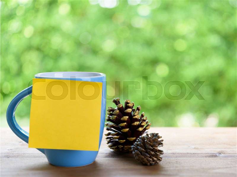 Blue coffee cup,post it for text and pine corn on wood table top with nature green blurred background, stock photo