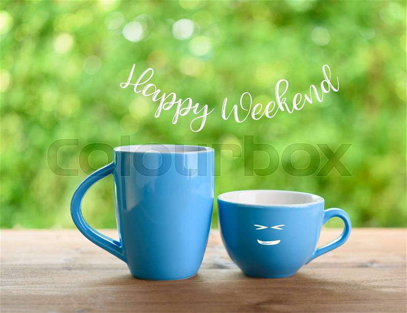Blue coffee cups and happy weekend text on nature green blurred background, stock photo