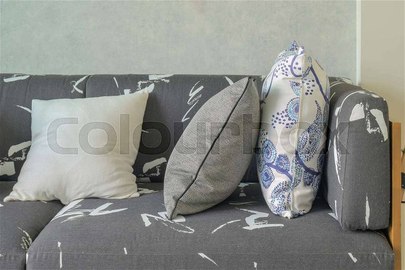 Decorative pillows setting on gray sofa with wooden base in living room, stock photo