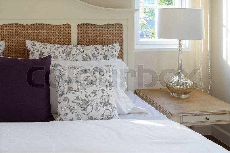 Vintage bedroom interior with flower pillows and decorative table lamp, stock photo