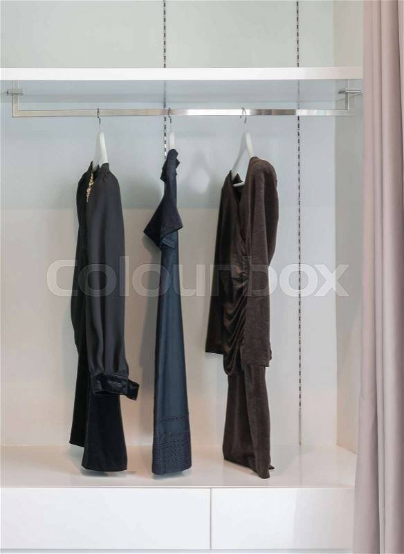 Modern closet with row of black dress hanging on coat hanger in wardrobe, stock photo