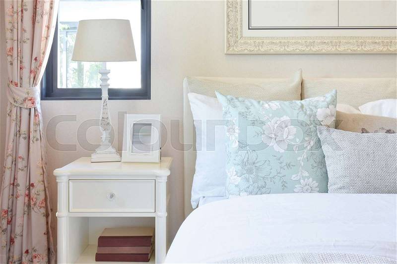 Vintage bedroom interior with reading lamp and picture frame on white bedside table, stock photo