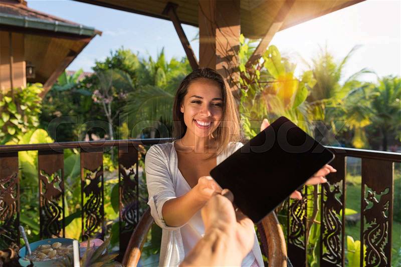 Pov Of Man Giving Woman Tablet Computer With Empty Blank Screen, Beautiful Young Girl Hold Digital Pc Sitting Outdoors On Summer Terrace In Tropical Forest, stock photo