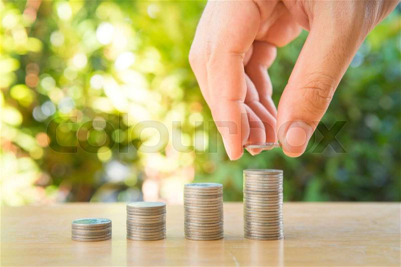 Human hand is putting coin to growing coin stack with nature background for saving money concept, stock photo