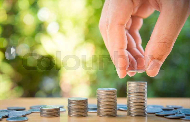 Human hand is putting coin to growing coin stack with nature background for saving money concept, stock photo