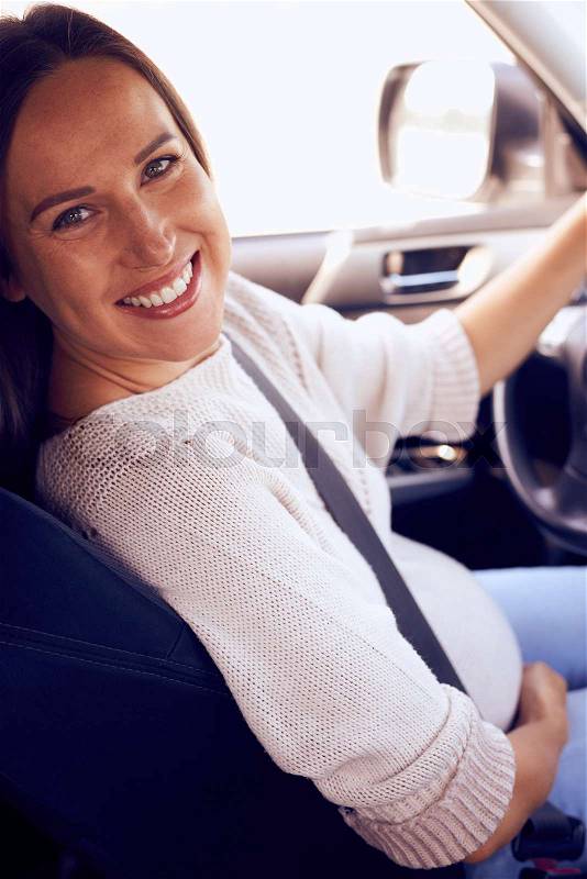 Closeup of pregnant woman sitting at wheel turning back to the passenger, stock photo