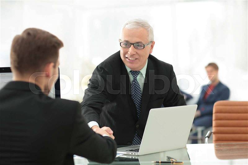 Businessman welcomes business partner shaking hands sitting behind a Desk in a modern office, stock photo