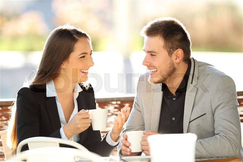 Two executives talking during a cofee break sitting in a bar terrace with a warm backlight, stock photo