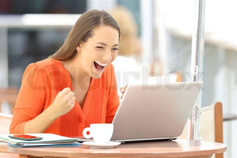 Single excited entrepreneur receiving good news on line in a laptop sitting in a restaurant terrace, stock photo