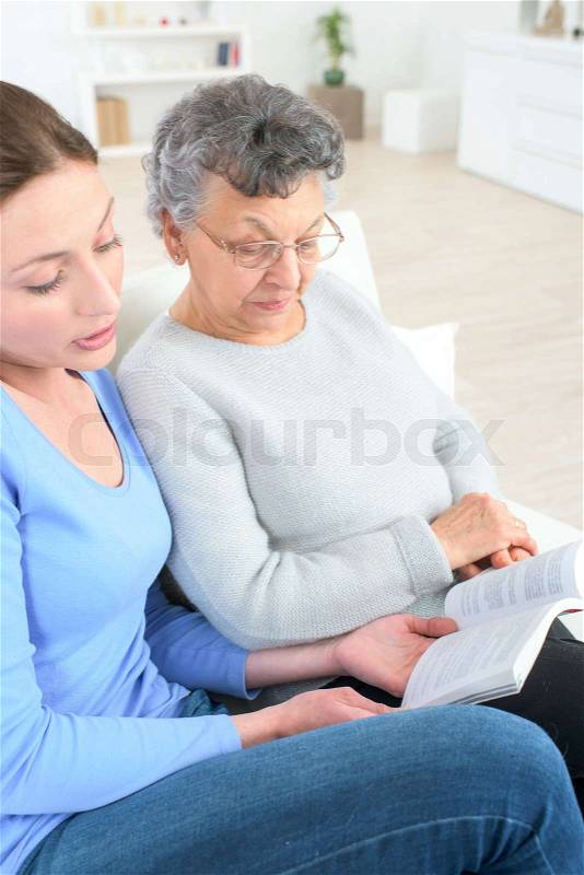 Grand daughter reading a book to her grandma, stock photo