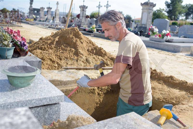 Caucasian man digging grave at cemetery, stock photo