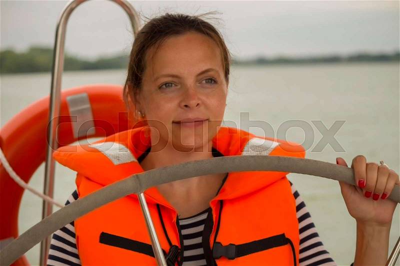 Cute young woman captain in the life jacket at the helm of the yacht, stock photo