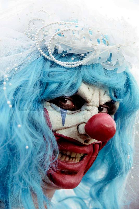 Closeup of a scary evil clown wearing a dirty and ragged bride dress outdoors, stock photo