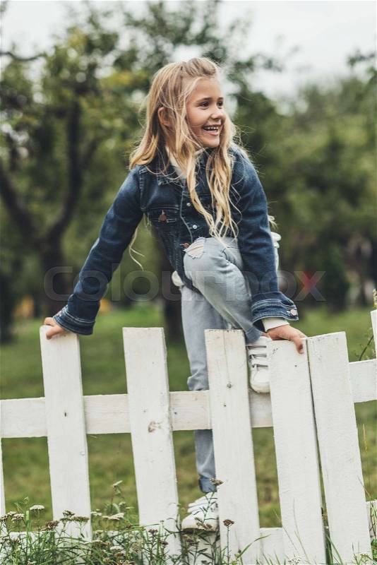 Adorable blonde child climbing over the fence at countryside , stock photo