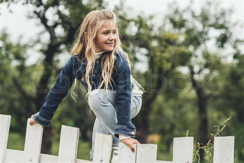Spring blonde child climbing over the fence at countryside , stock photo
