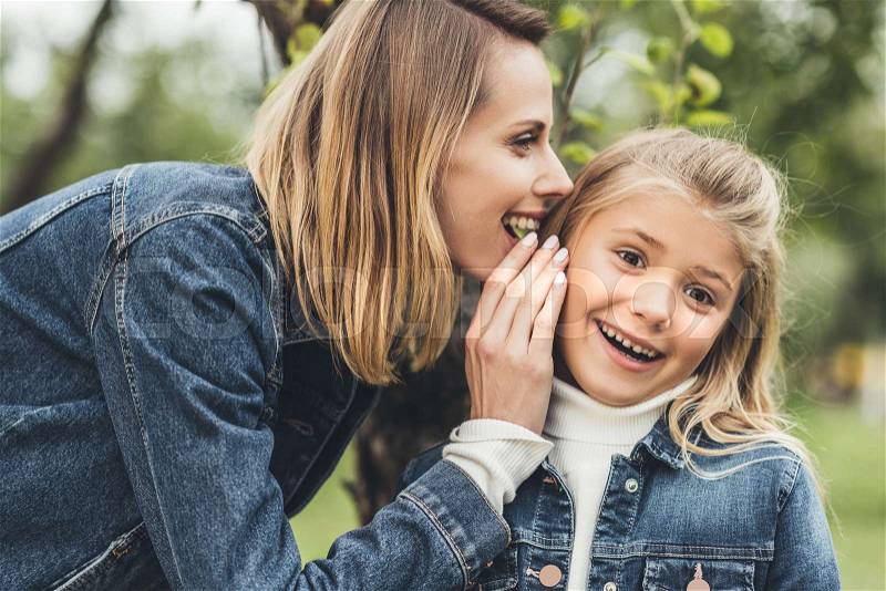 Happy mother whispering to her daughter at countryside, stock photo