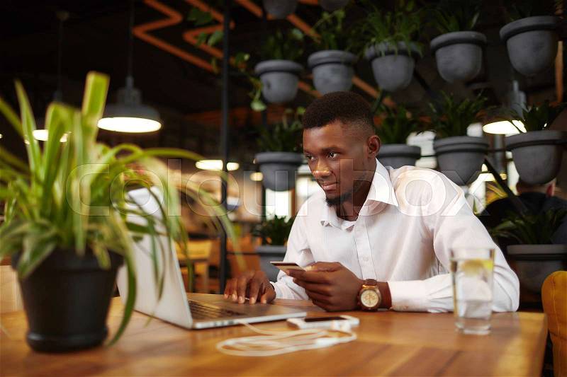 Young african man shopping, doing order at internet shop, pay with card typing on laptop, holding credit plastic card. Freelancer, businessman buying from internet, sending money. Stylish interior, stock photo