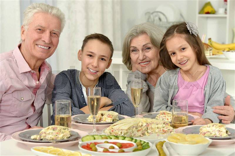 Brother and sister having breakfast together with their grandparents, stock photo