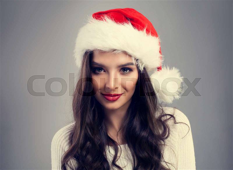 New Year Woman in Santa Hat. Christmas Fashion Model with Perfect Makeup and Long Healthy Curly Hair, stock photo