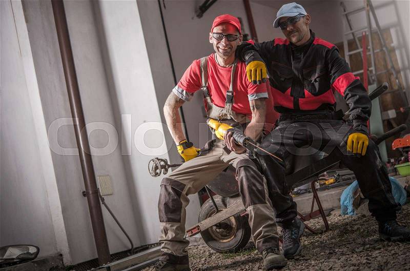 Pro Construction Crew. Two Caucasian Contractors in Front of the Residential Building. Small Business and Industrial Theme, stock photo