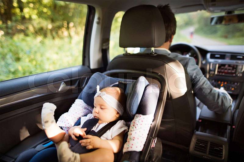 Unrecognizable man driving with a baby girl in car seat, stock photo