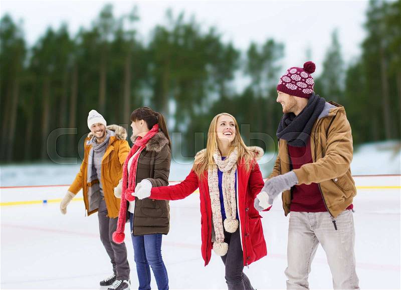 Friendship, winter and leisure concept - happy friends holding hands on skating rink over outdoor background, stock photo