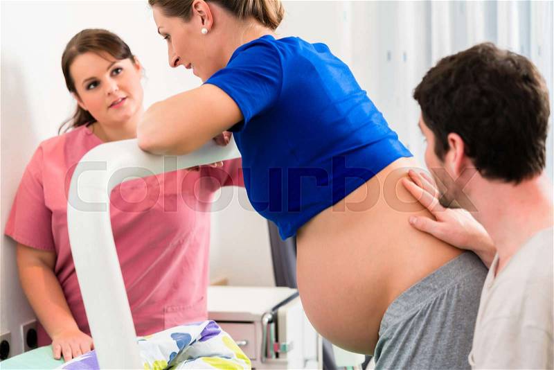 Woman laboring in delivery room with nurse and husband before birth, stock photo