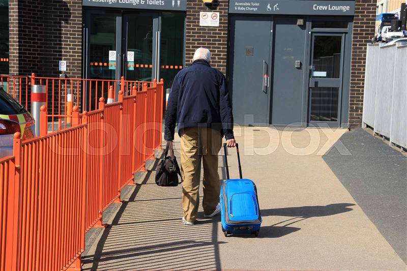 The elderly man is walking with his trolley suitcase to the coach in the city Glascow in Scotland in the summer, stock photo