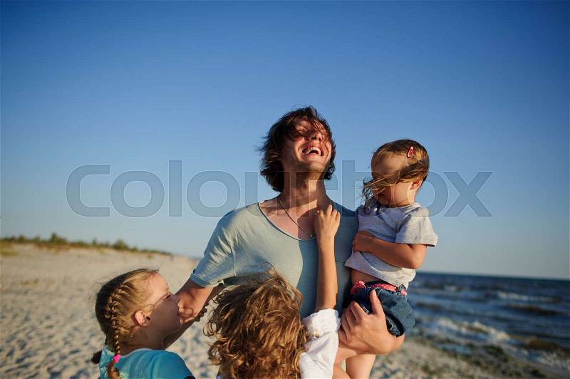 Dad is playing on the beach with three children. Everyone is very happy. The sun, the blue sky, the sea wind, stock photo