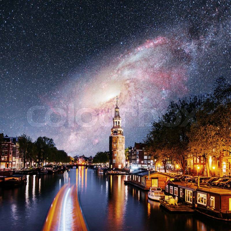 Beautiful night in Amsterdam. Night illumination of buildings and boats near the water in the channel. Fantastic starry sky and the milky way. Courtesy of NASA. , stock photo