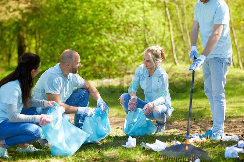 Volunteering, charity, people and ecology concept - group of happy volunteers with garbage bags and rake cleaning area in park, stock photo