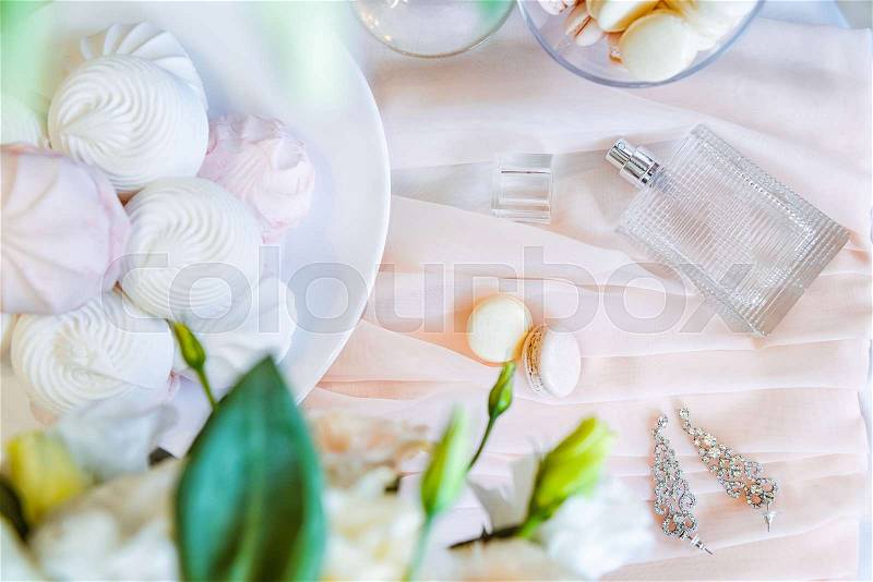 Bridal morning details composition. Top view of bride\'s jewelery, perfumes, bouquet of eustoma flowers and marshmallow and macaroon sweets. Flat lay. Selective focus. Space for text, stock photo