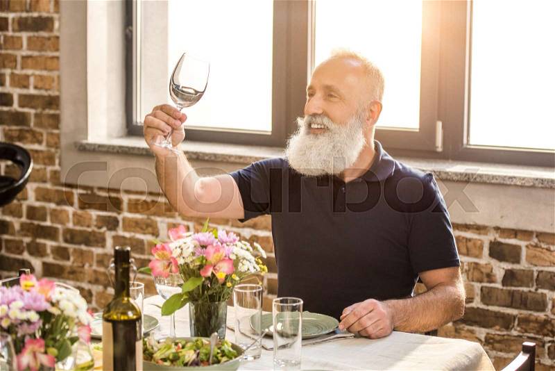 Portrait of senior man looking at empty wine glass in hand, stock photo