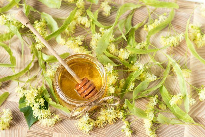 Honey in glass jars with white linden flowers on light wooden background. Shallow depth of field, stock photo