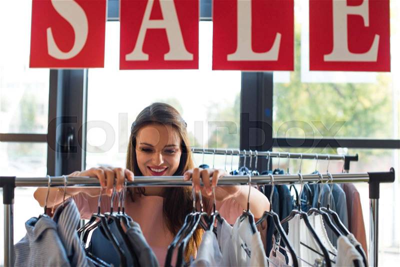 Happy young woman looking at stylish clothes in boutique, stock photo