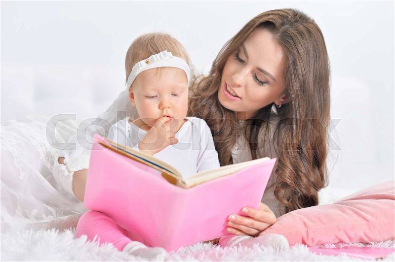 Beautiful young mother with cute little daughter reading book, stock photo