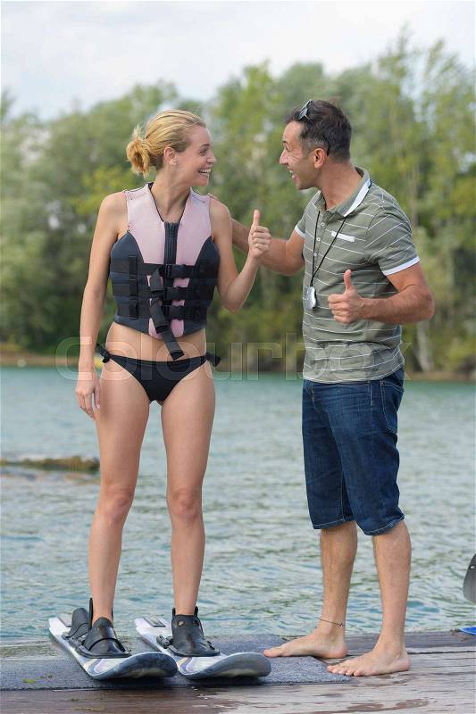 Happy young girl learning how to water ski with coach, stock photo