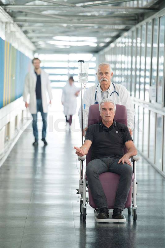 Patient in a wheelchair pushed by doctor in hospital, stock photo