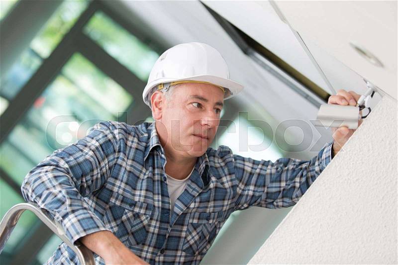 Male technician installing camera on wall, stock photo