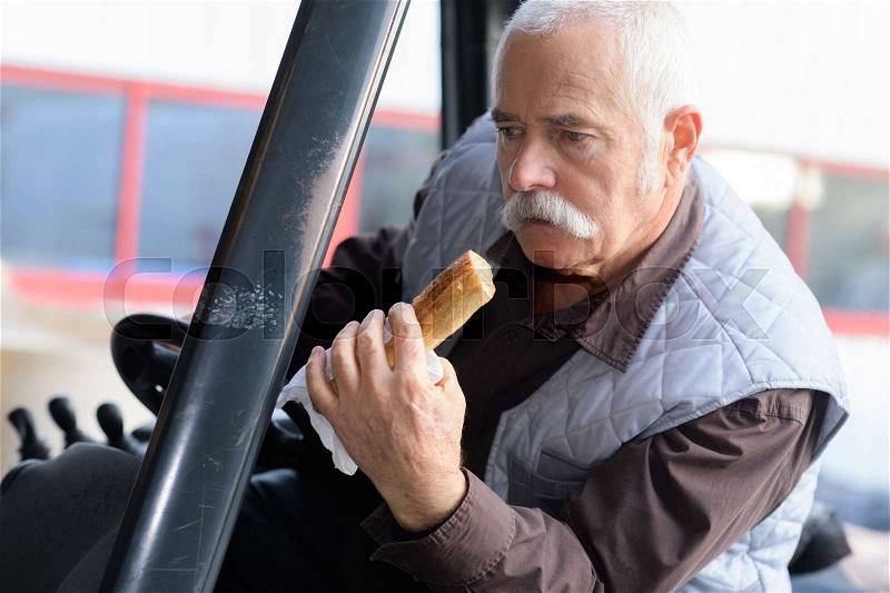 Driver eating bread while driving a classic tractor, stock photo