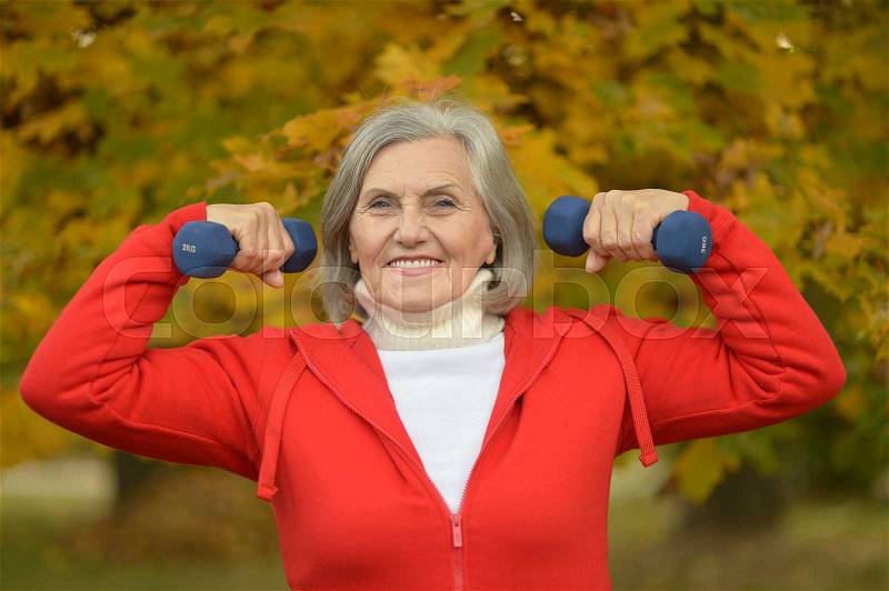 Happy fit senior woman exercising in autumn park with dumbbells, stock photo
