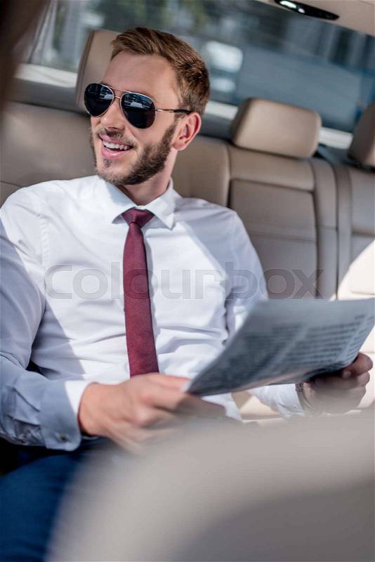 Young businessman in sunglasses with newspaper on backseat of car, stock photo