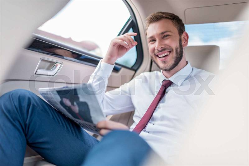Happy young man with newspaper on backseat of car, stock photo